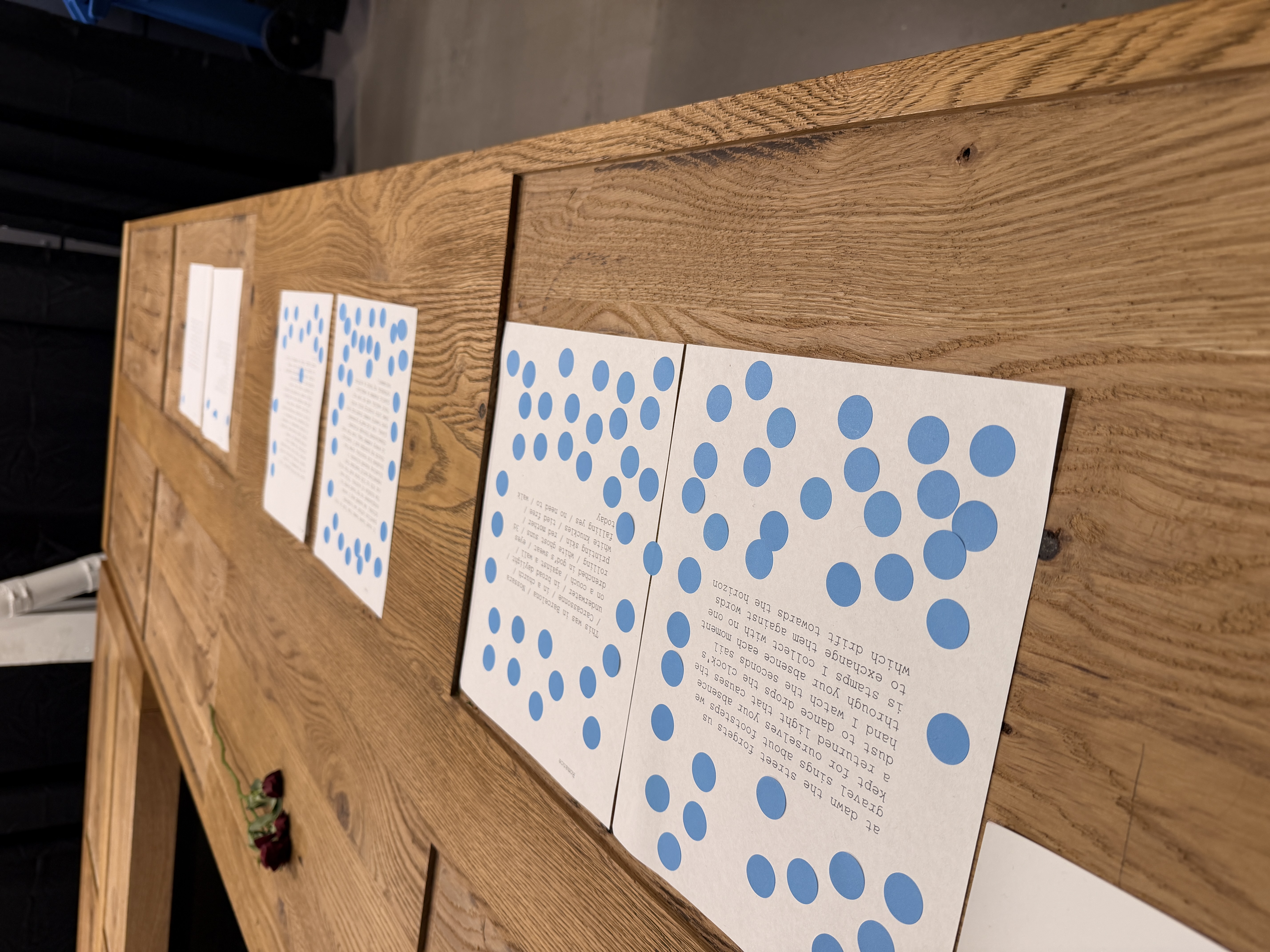 Poems lined up along a wooden ledge with blue stickers accumulating