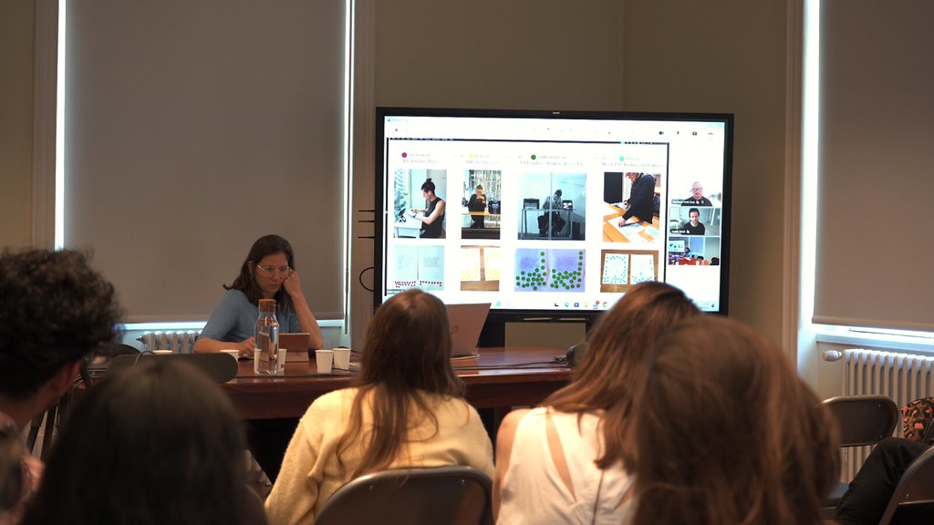 The room at the Instituto de Literatura Comparada during recover.exe - the audience watches the venue screen, Halim streamed in on camera beside the anonymized poems