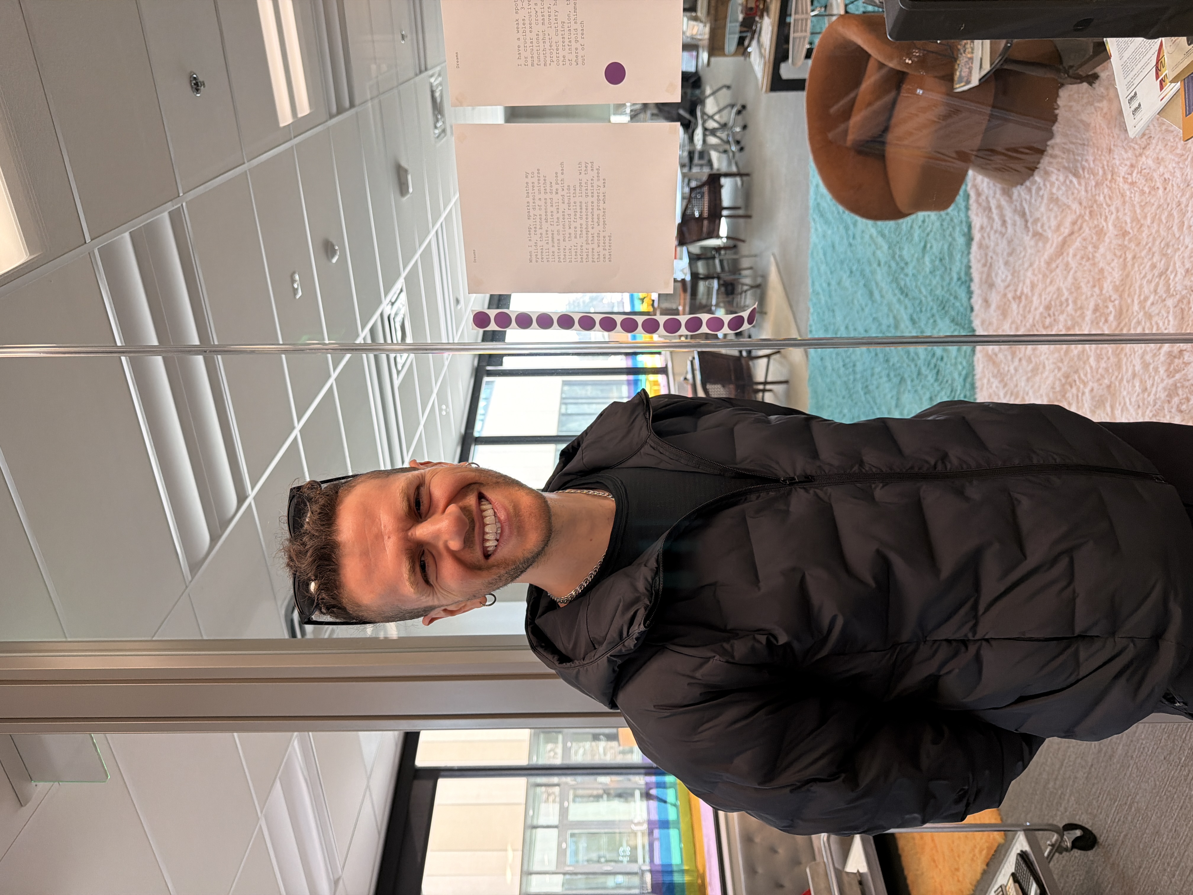 The poet smiling at the Media Archaeology Lab with poems and stickers on the wall behind