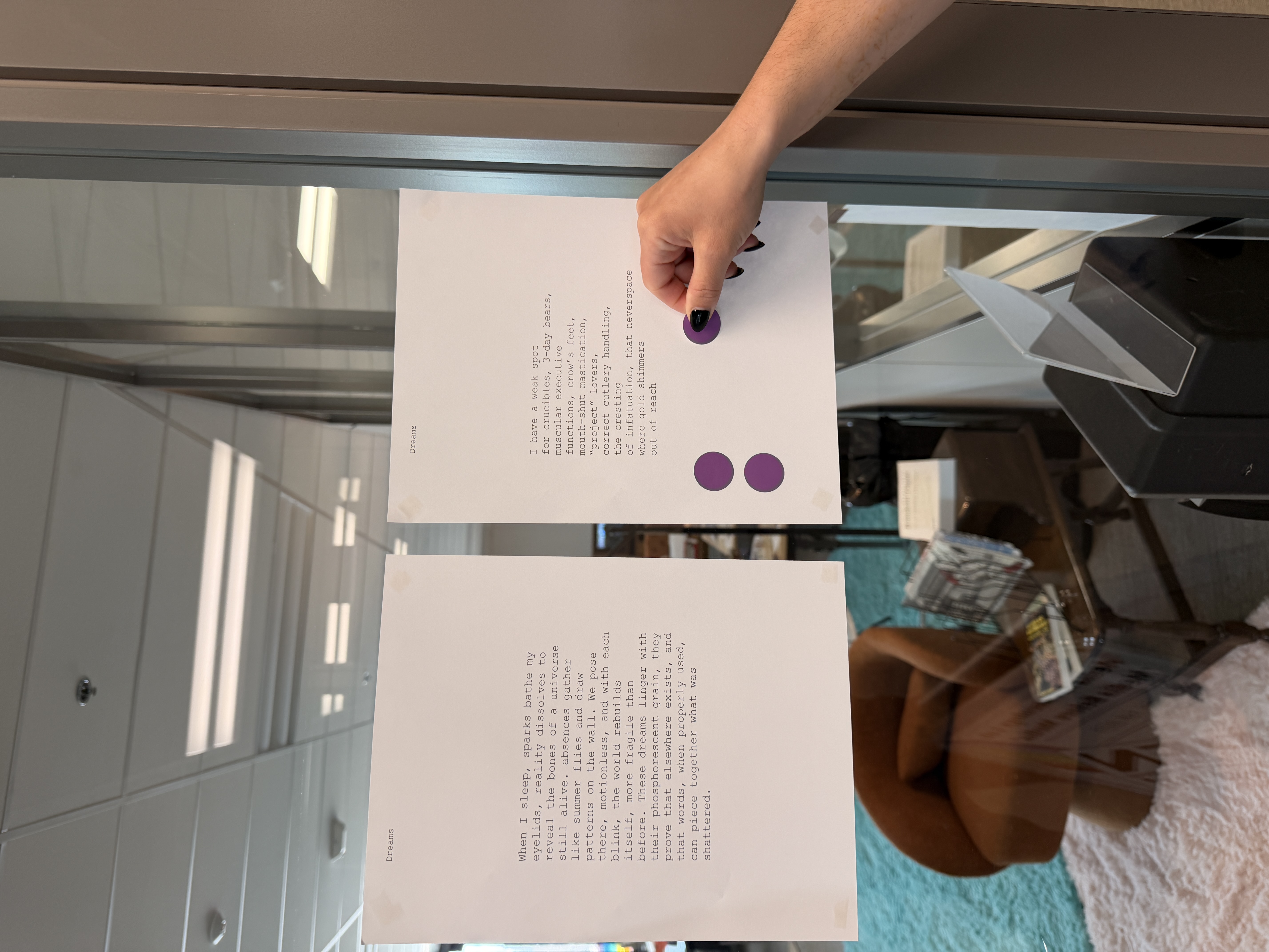A hand placing a purple voting sticker on printed poems